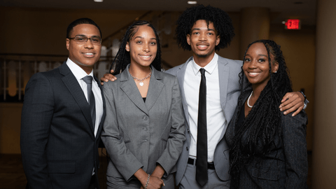 Four law students in professional attire representing clinics and externship programs, standing together and smiling.