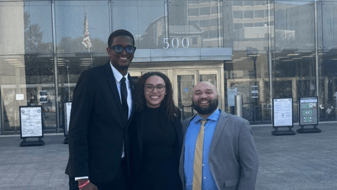 Three individuals in professional attire standing outside a courthouse, representing the Criminal Justice Clinic.
